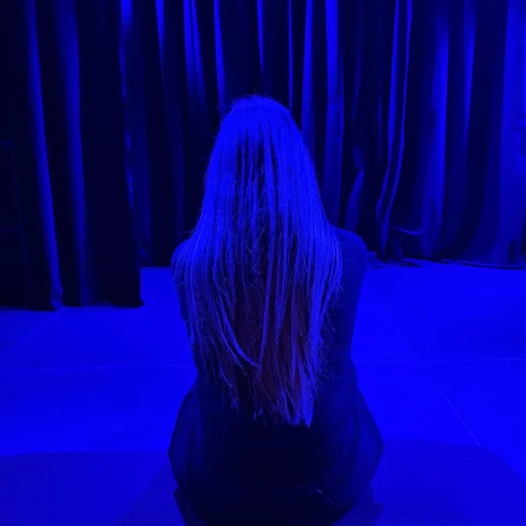 Sitzende Frau von hinten in blauem Licht. 