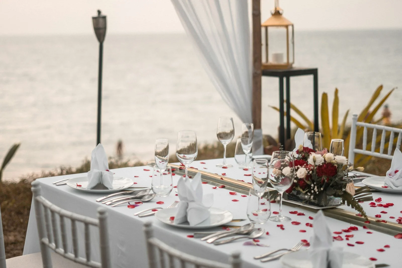 A dinner table set on the beach with the ocean behind it
