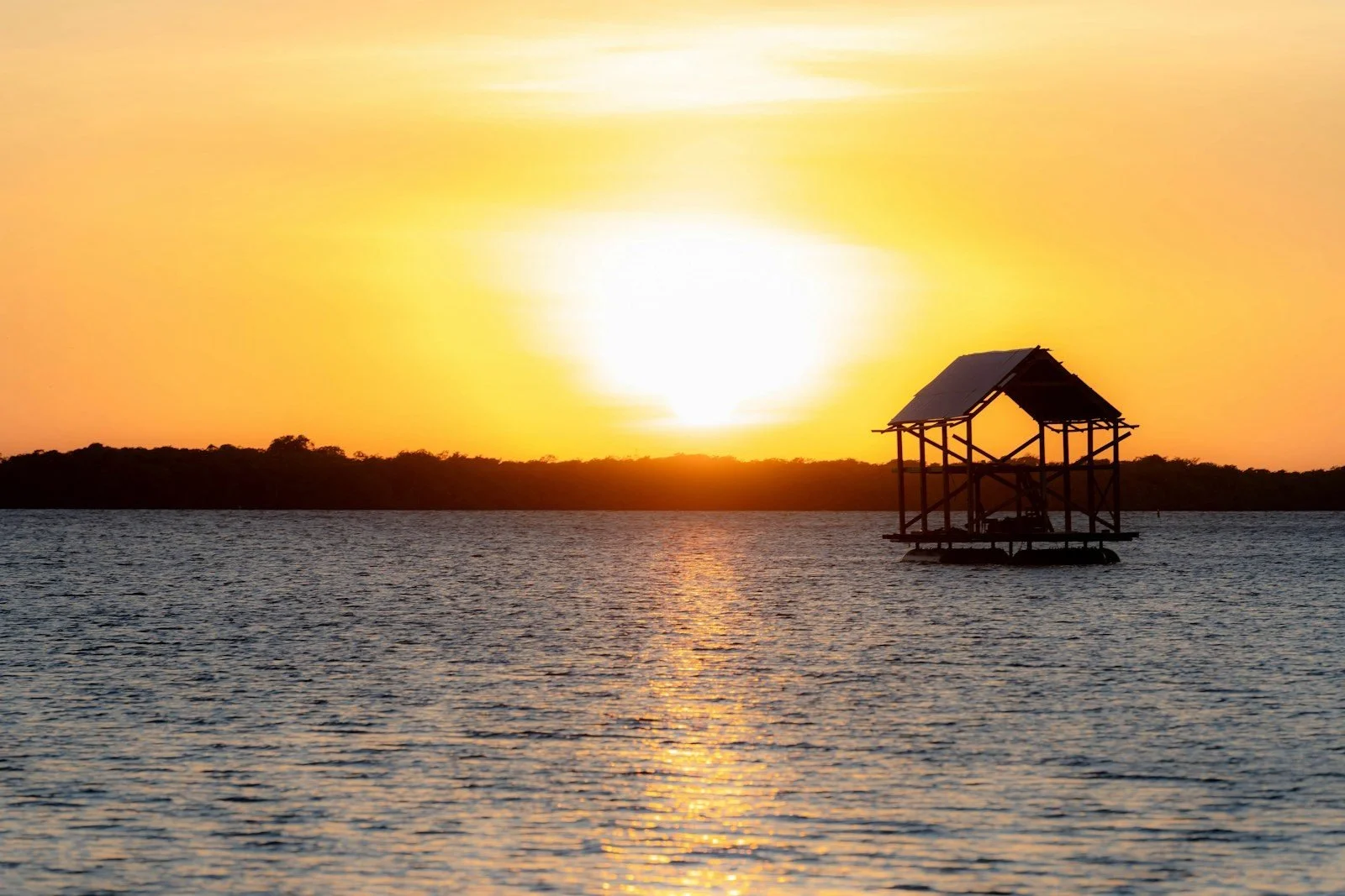 The sun setting behind a palapa over calm water