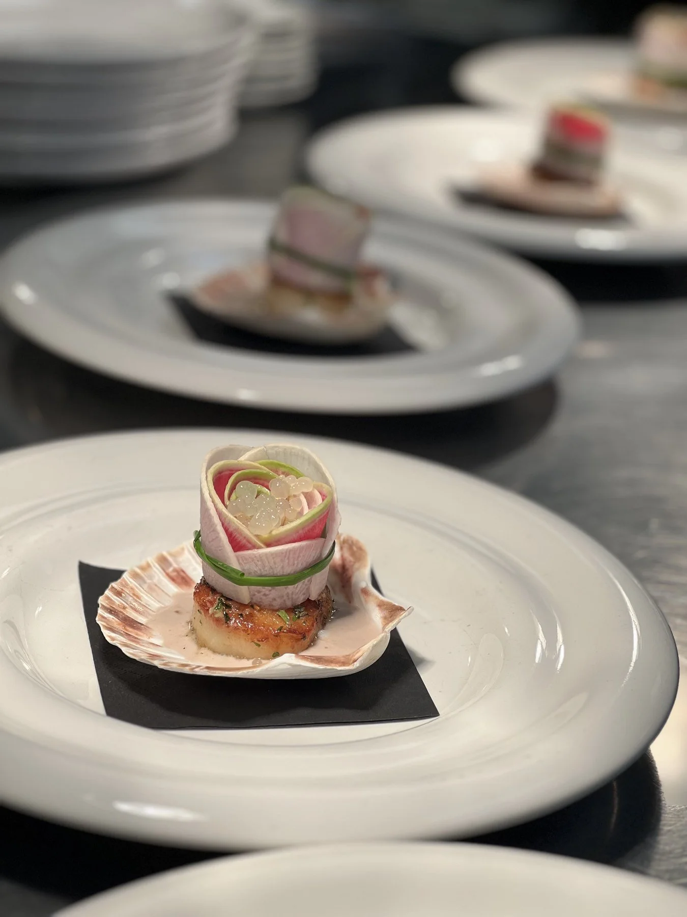 A seared scallop presented in its shell with delicate pink and green vegetable ribbons