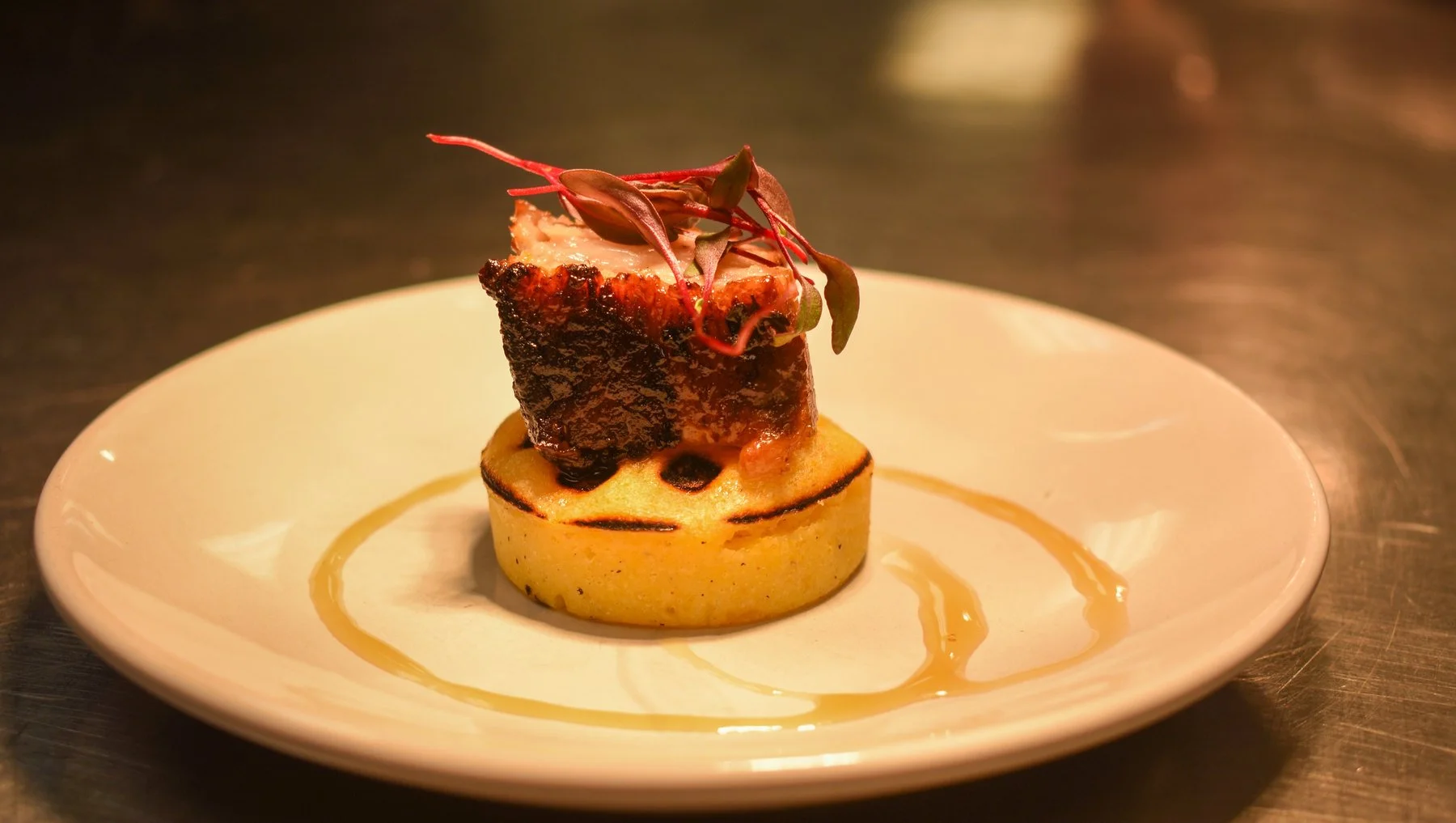 A seared entrée on a golden round base, finished with microgreens and a ring of sauce