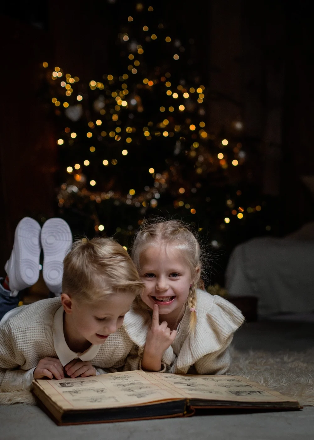 Zwei Kinder mit einem Buch vor dem Weihnachtsbaum
