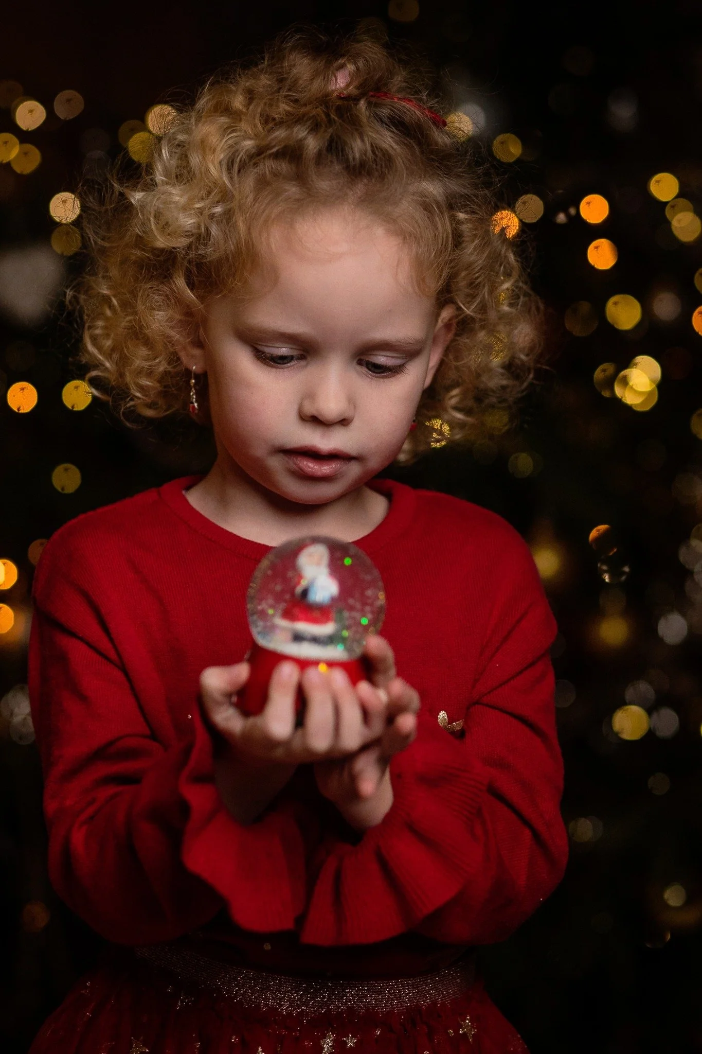 Kind mit Weihnachtskugel und goldenen Lichtern beim Weihnachtsshooting