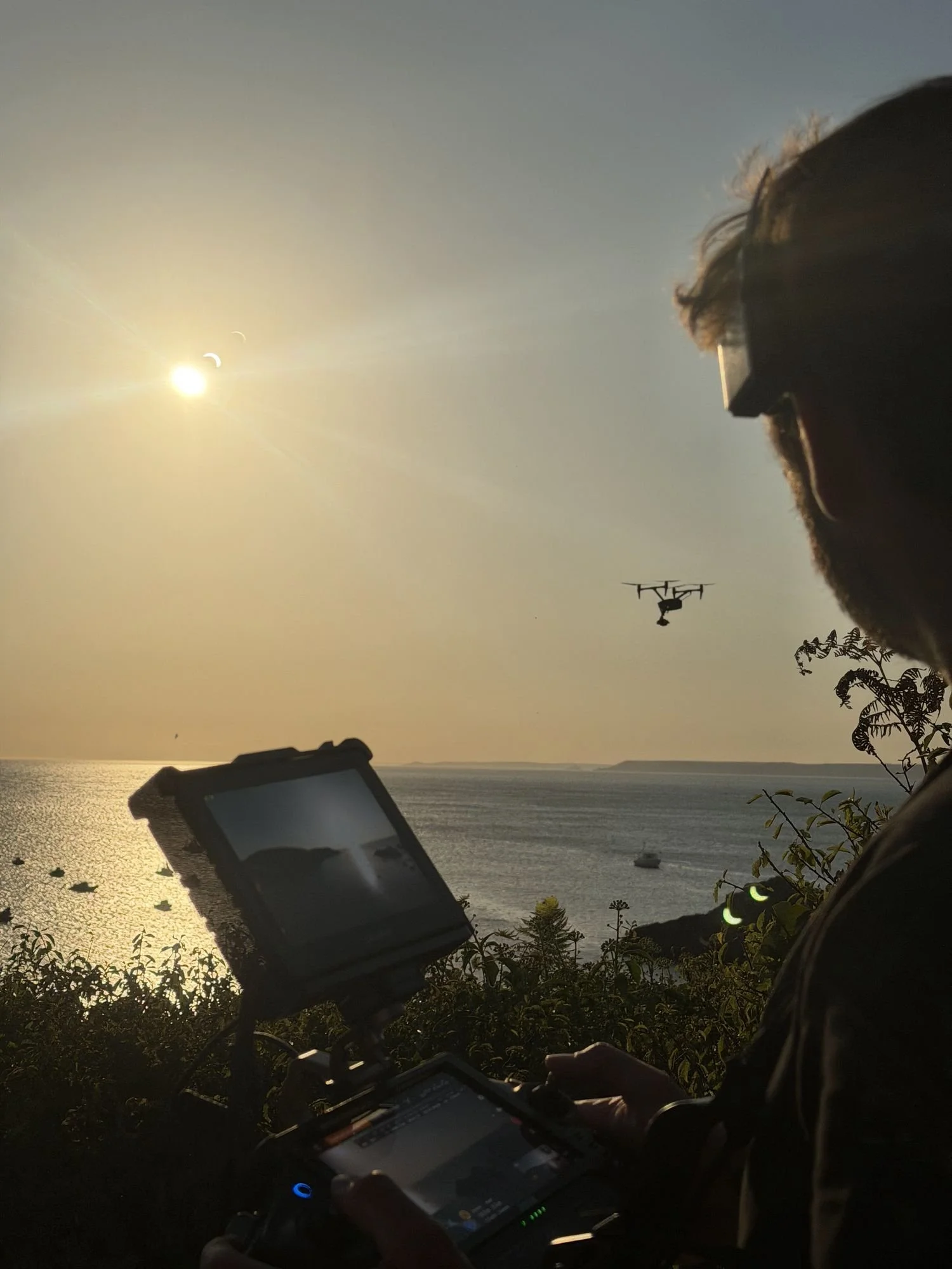 Drone pilot watching the monitor at sunset as the DJI Inspire 3 flies over the coast