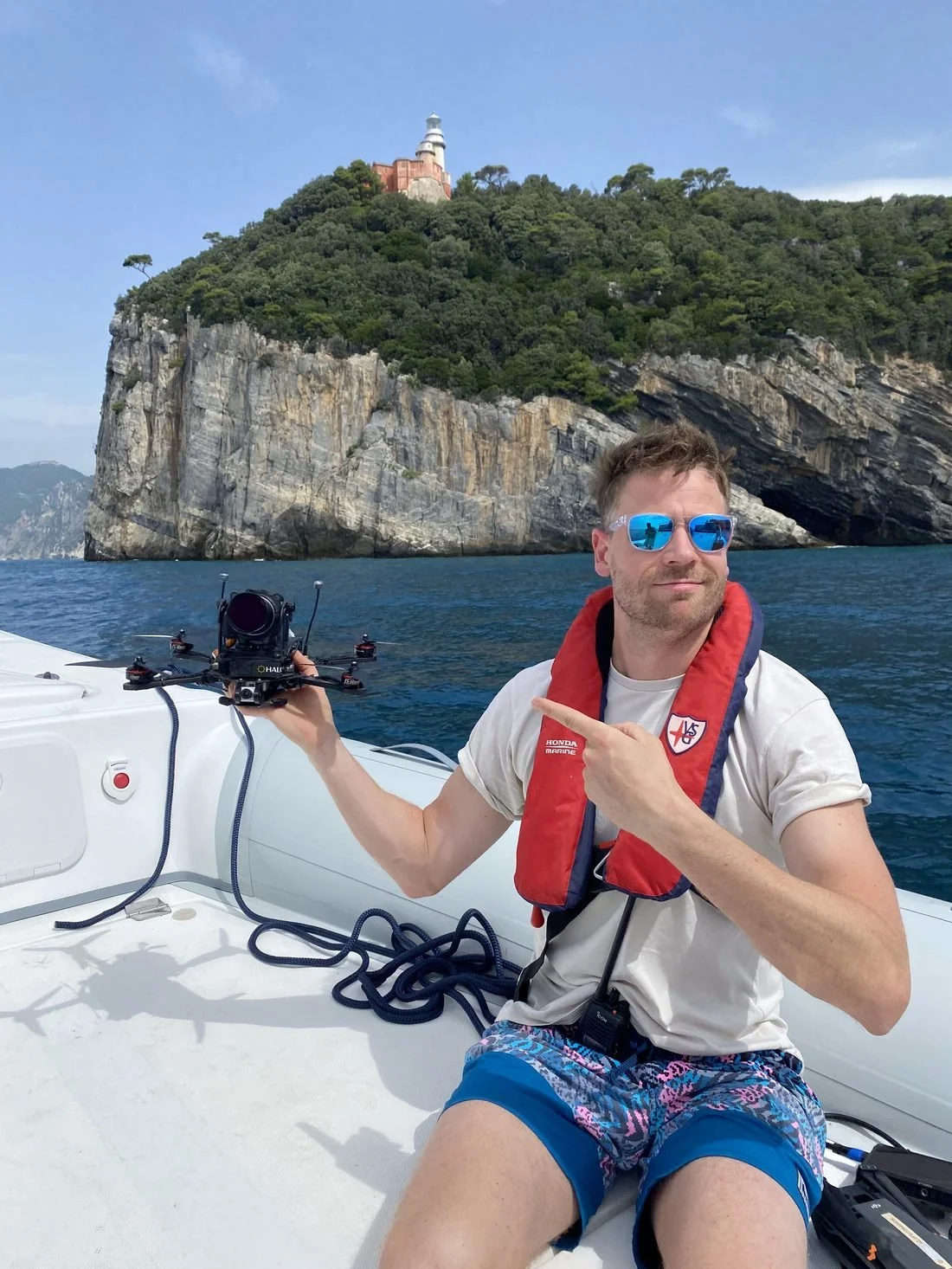 FPV pilot holding a cinelifter drone on a boat below sea cliffs