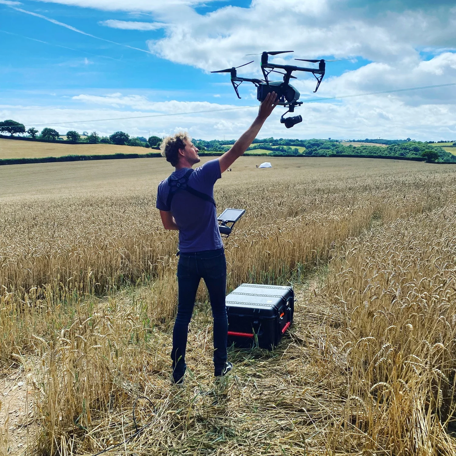 Pilot hand-catching a DJI Inspire 2 with Zenmuse X7 in a wheat field, flight case beside him