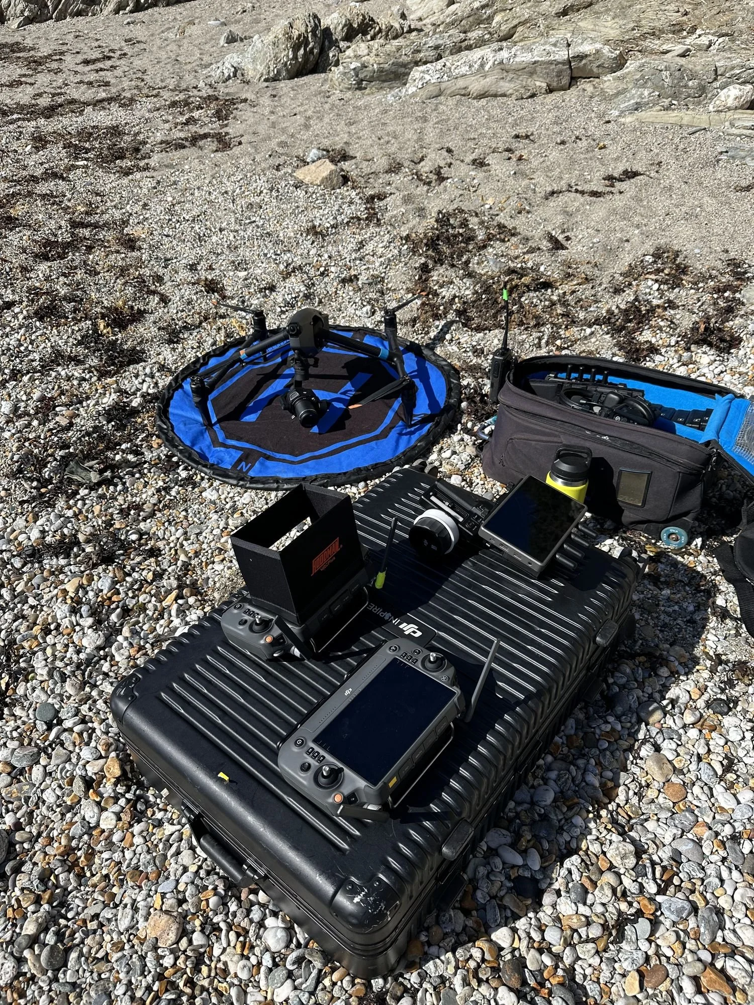 DJI Inspire 3 kit laid out on a beach: aircraft on landing pad, flight case, RC Plus controllers and monitor