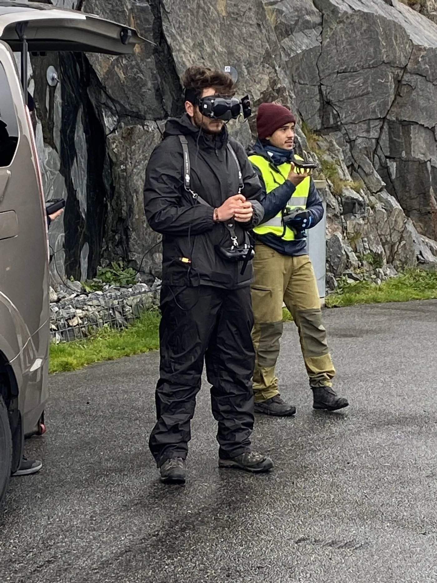 FPV pilot in goggles with a spotter in hi-vis on location