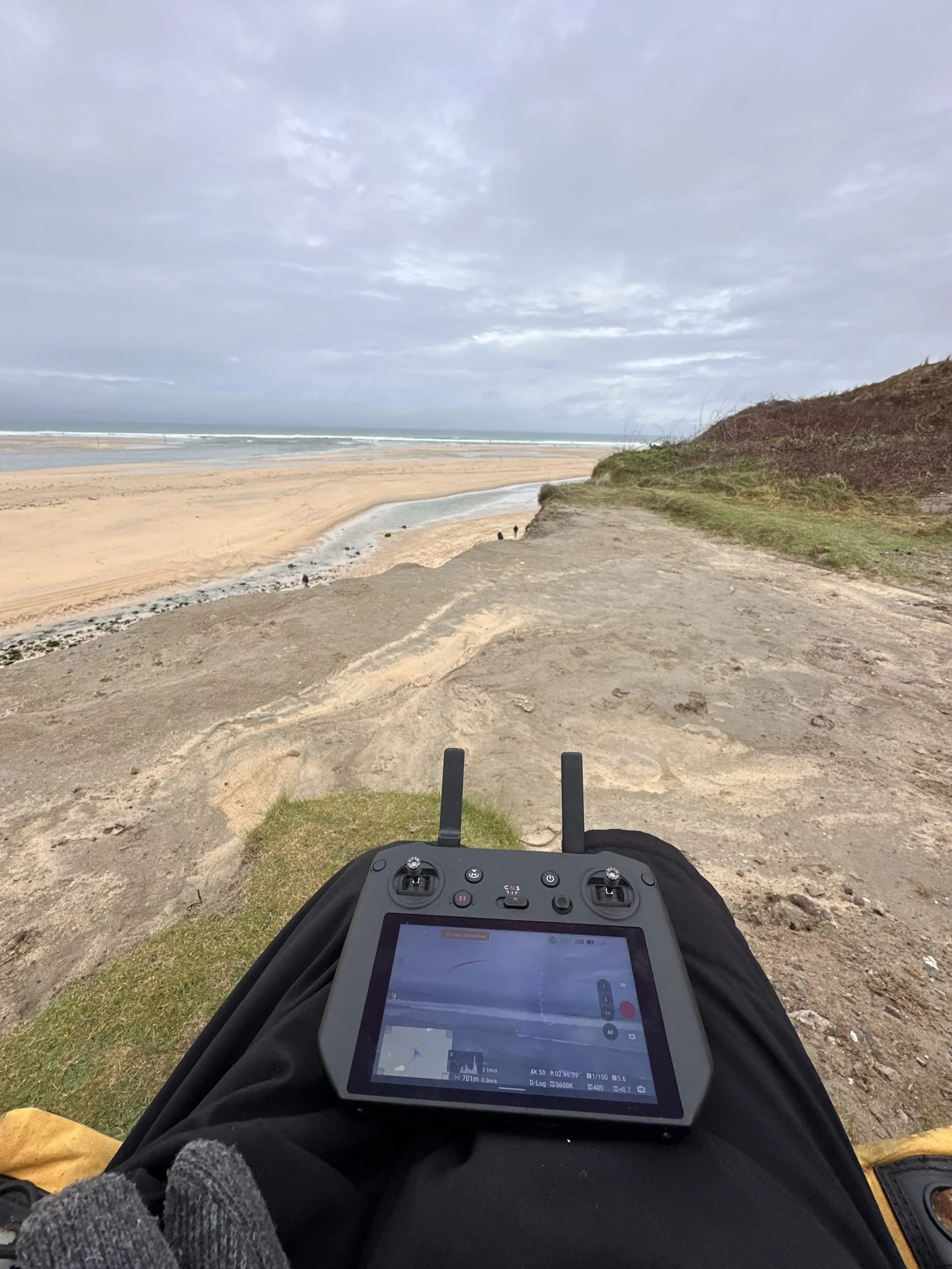 Mavic pilot on a Cornish clifftop with the controller, above a beach