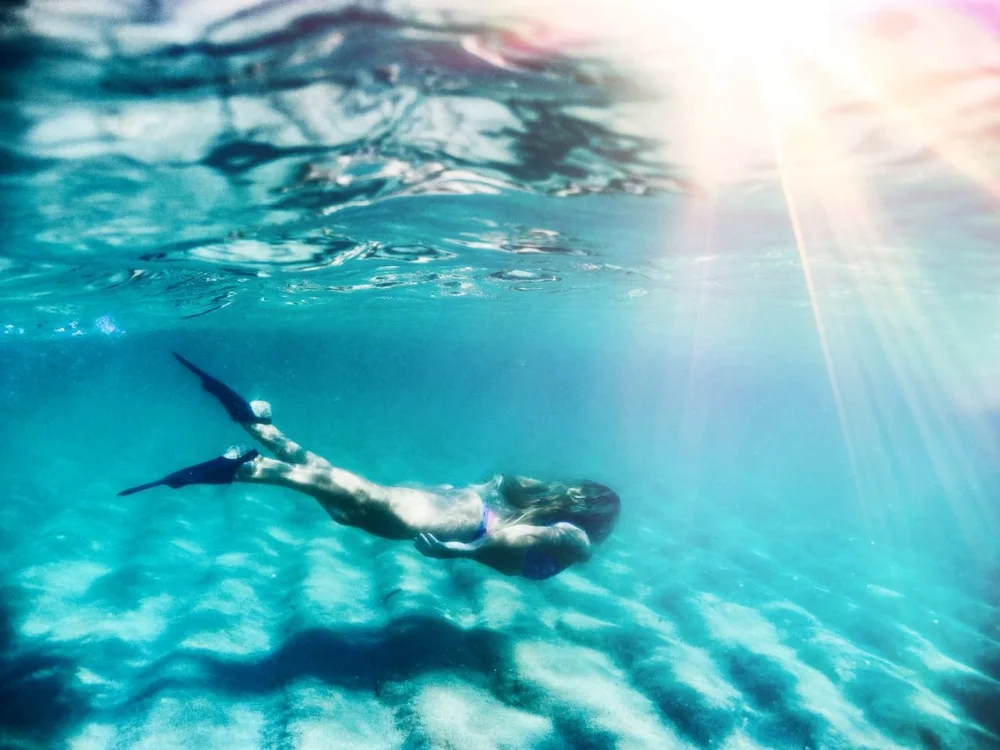 Freediver underwater with sun rays coming through the surface