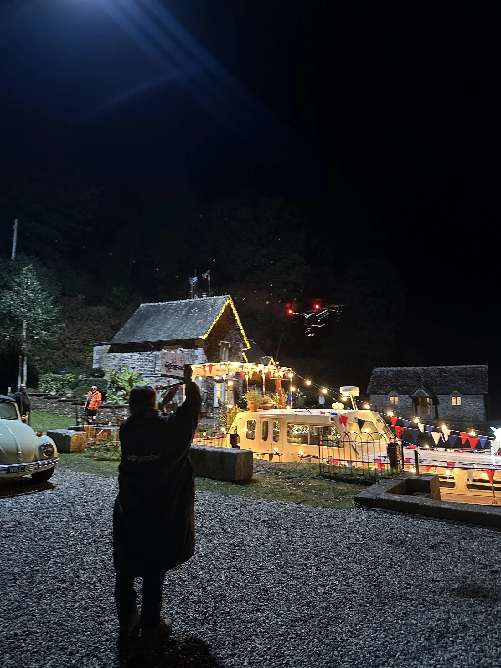 Drone light hovering over a village film set at night with a crew member directing it