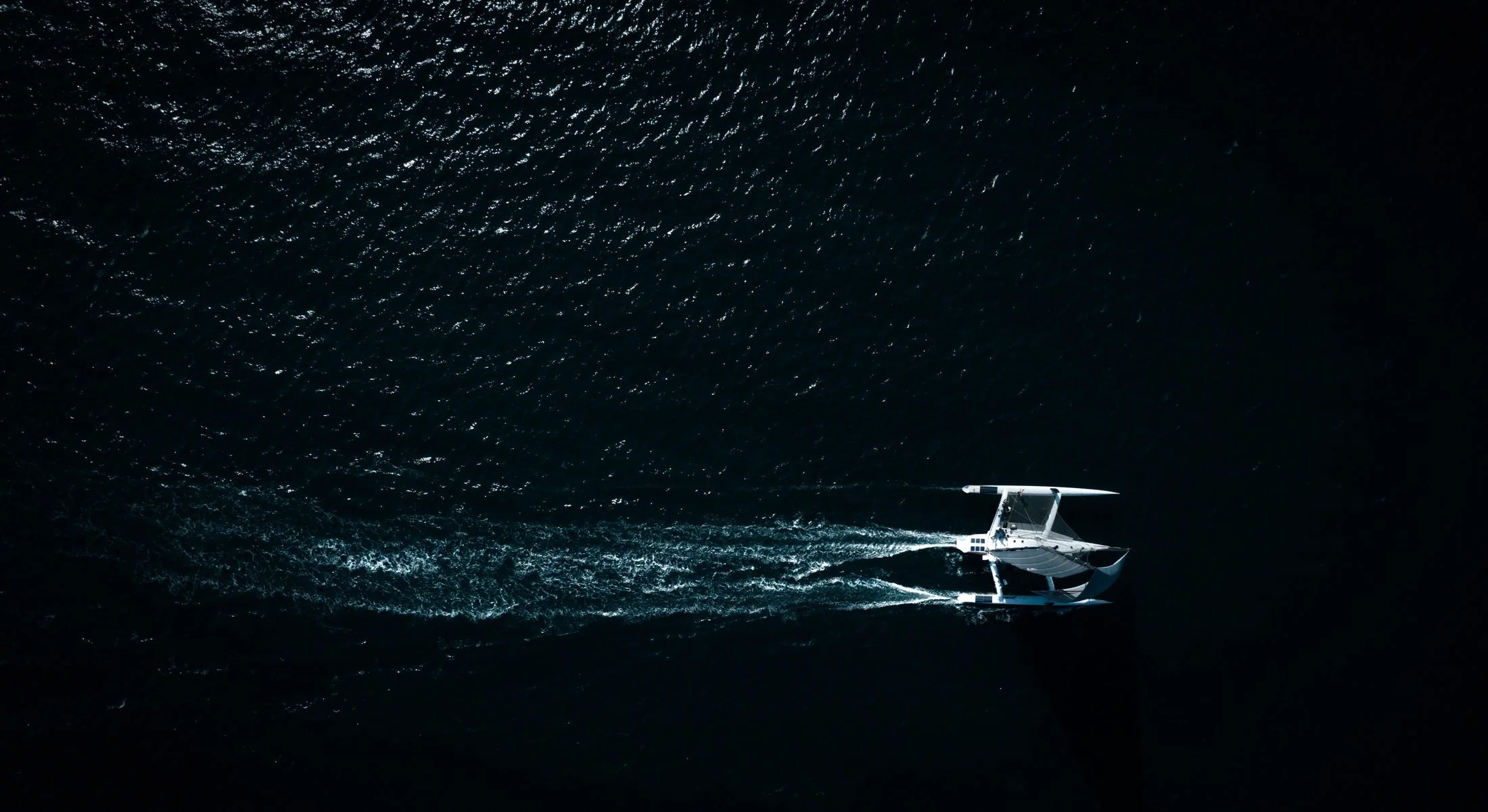 Trimaran Paradox crossing dark water off Cornwall, filmed from above with a DJI Mavic drone