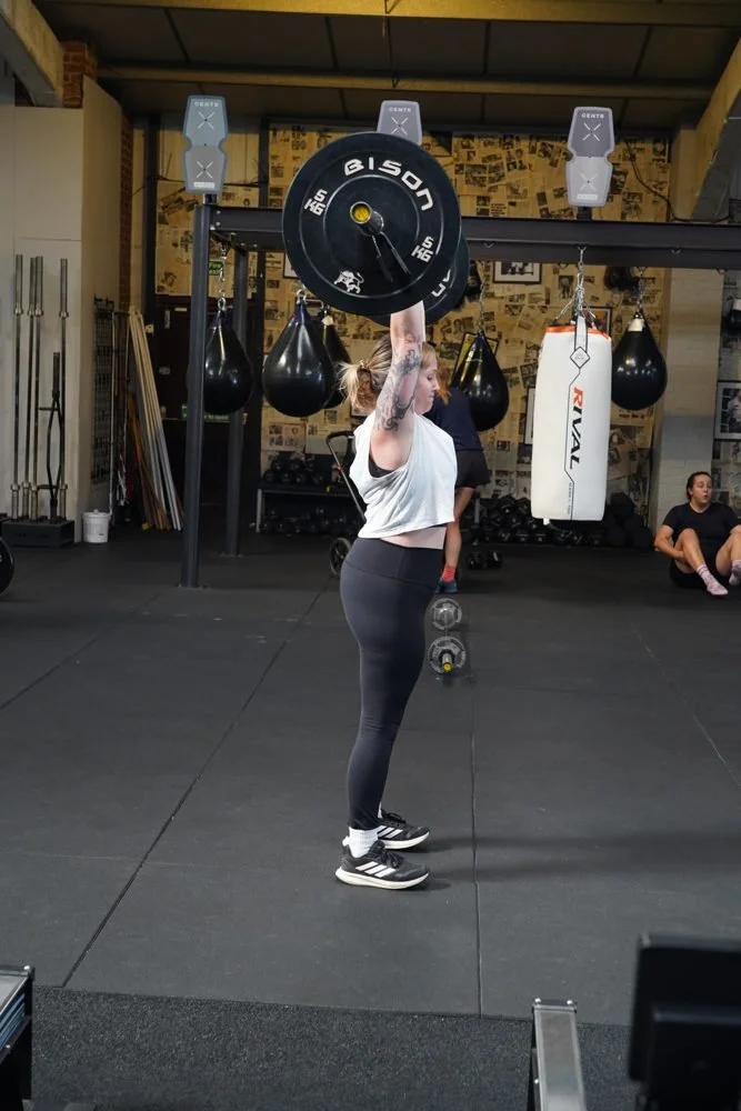 Member lifting a barbell overhead in a strength class