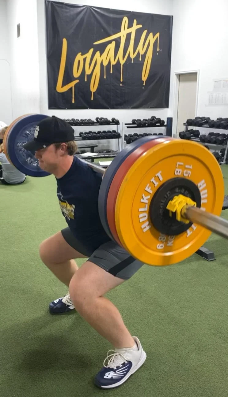 Athlete back squatting in front of the Loyalty banner