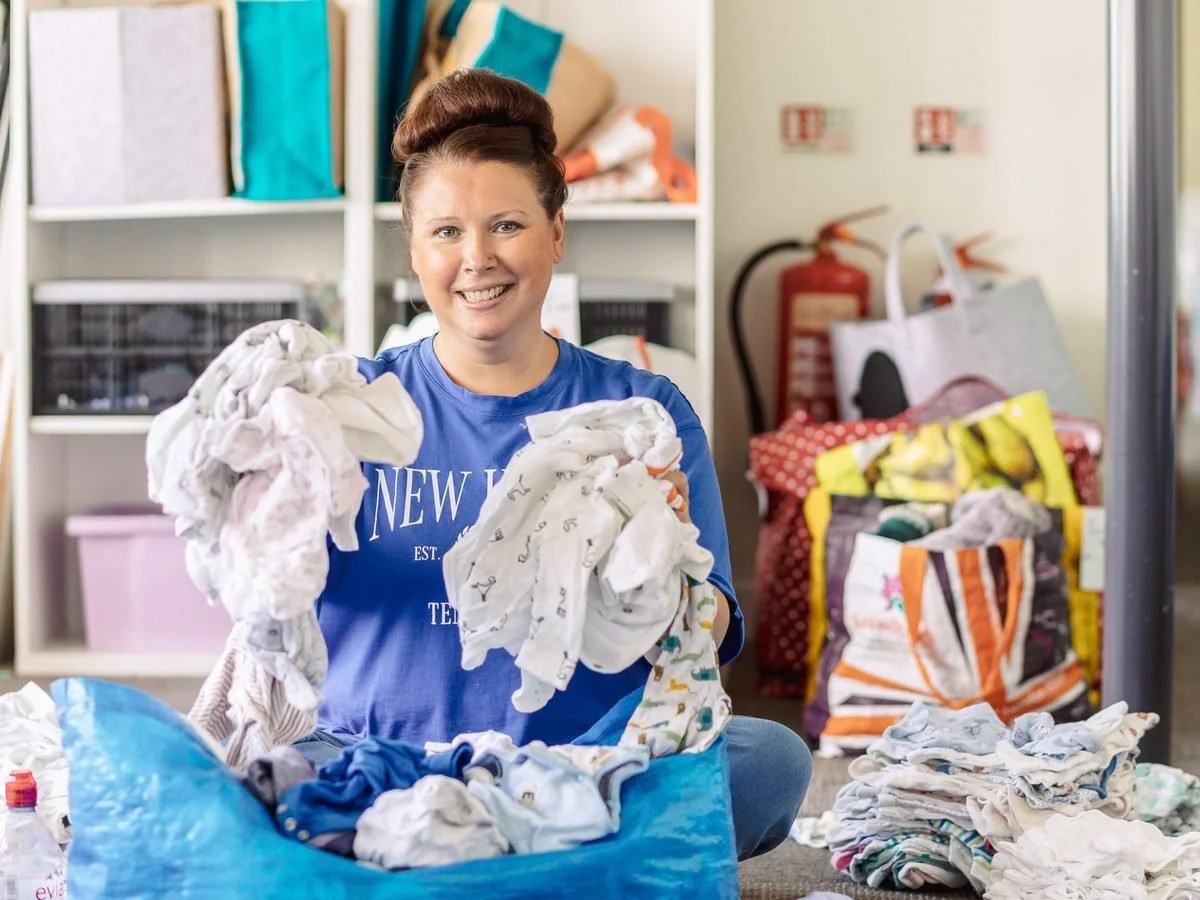 A volunteer sorting baby clothes from a donation bag