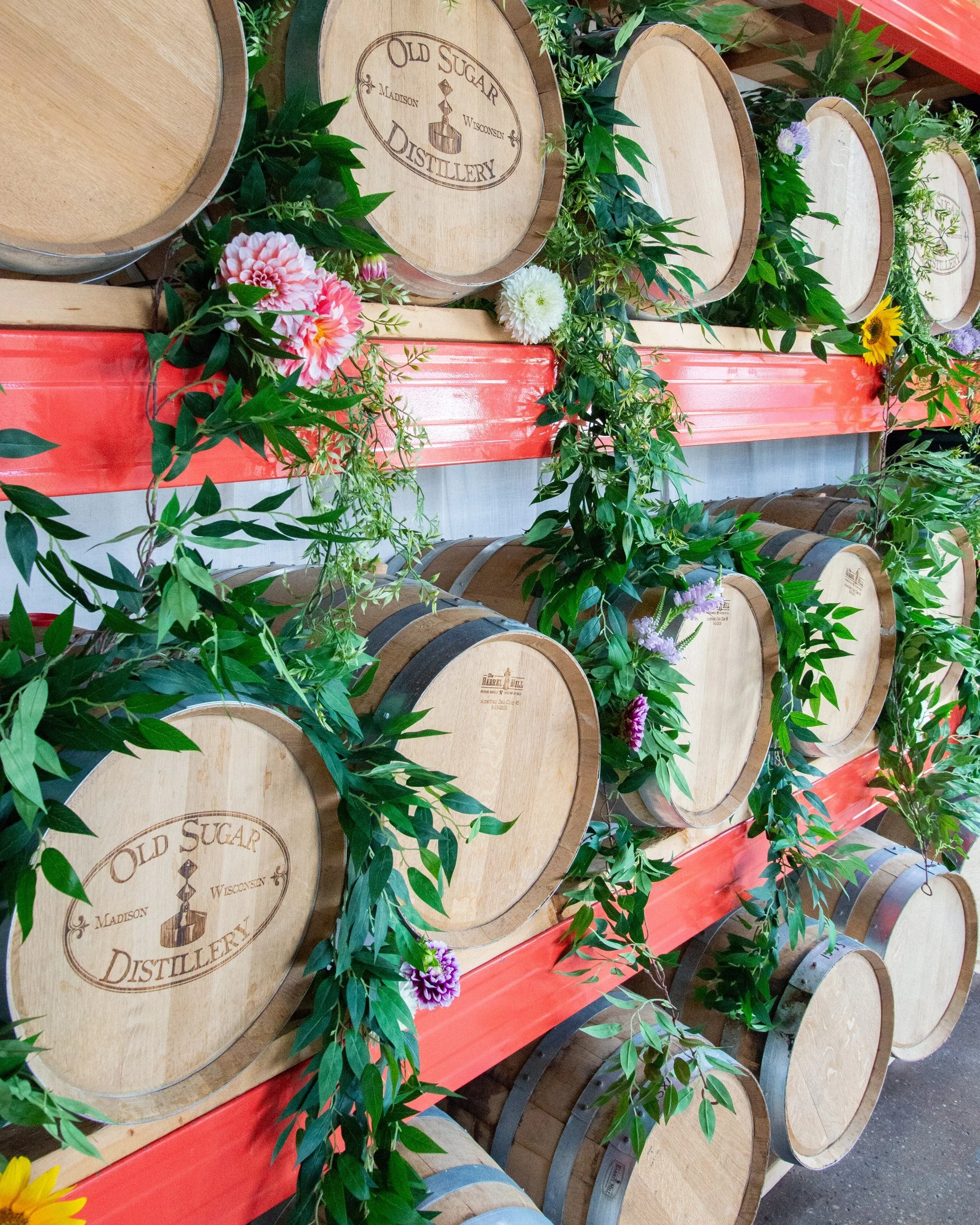 Floral arrangements and greenery decorating Old Sugar Distillery's barrel racks