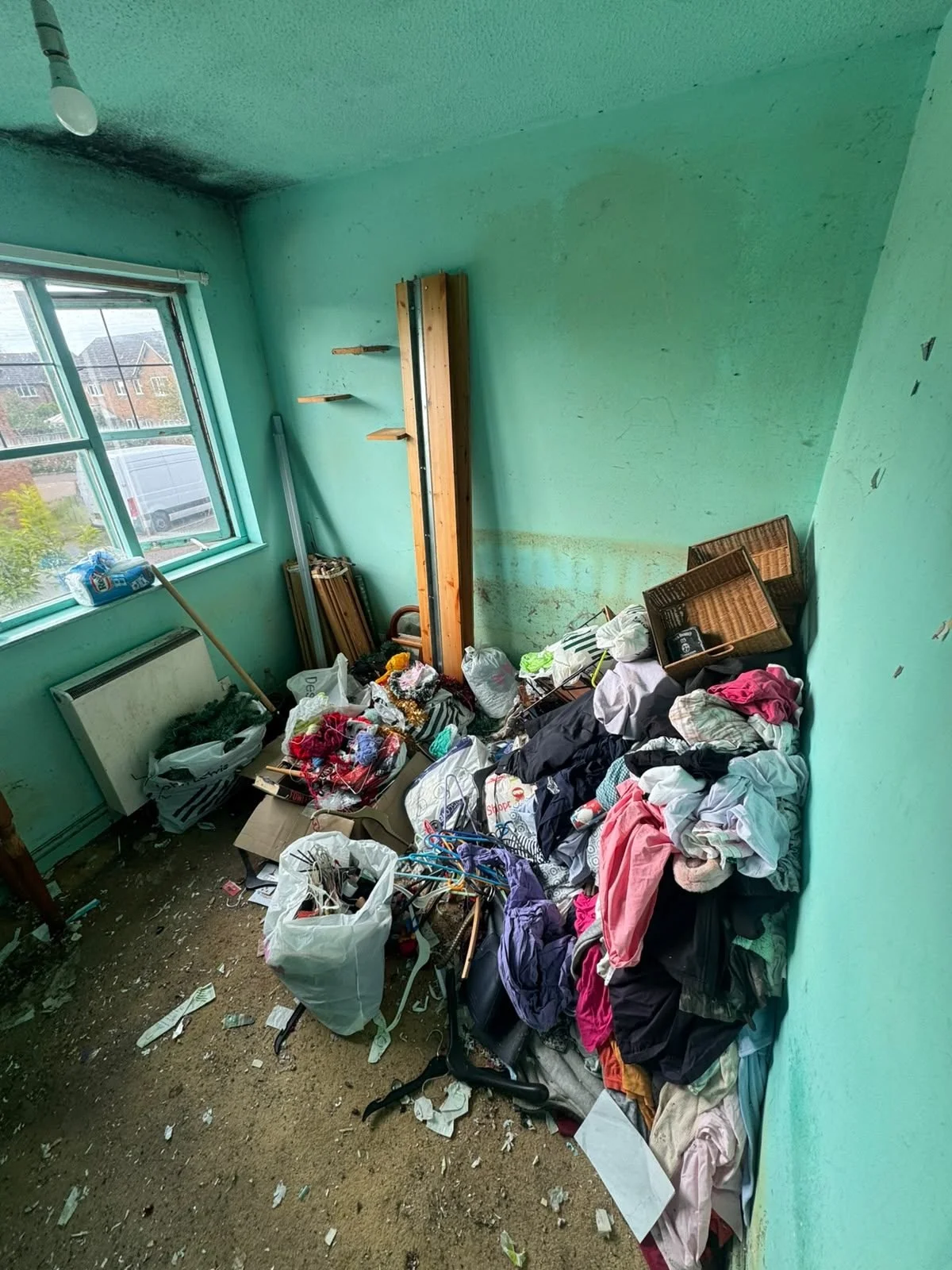 Hoarded bedroom before cleaning, floor covered with clothing and clutter