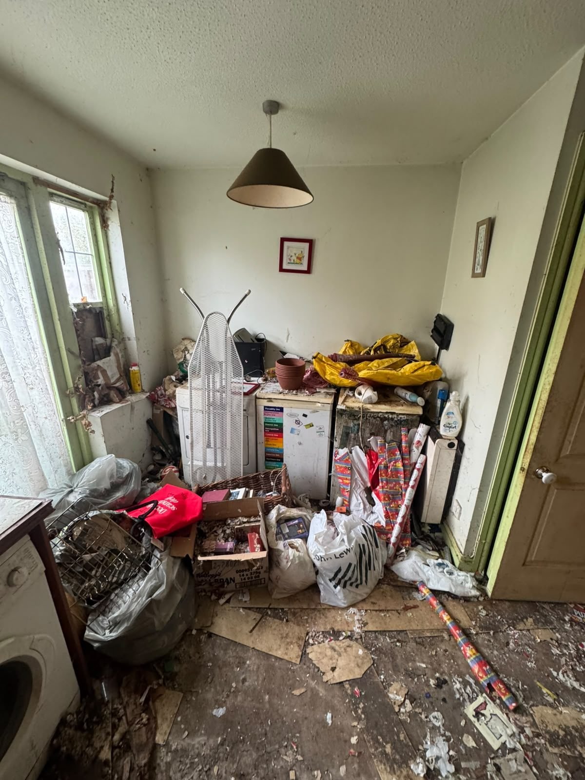 Hoarded kitchen before cleaning, clutter piled around the appliances and across the floor