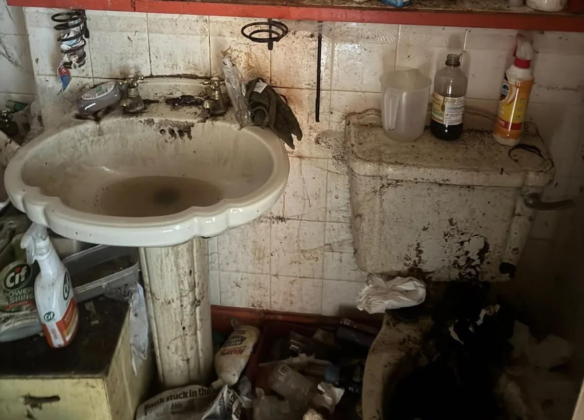 Hoarded bathroom before cleaning, heavily soiled sink and toilet with clutter