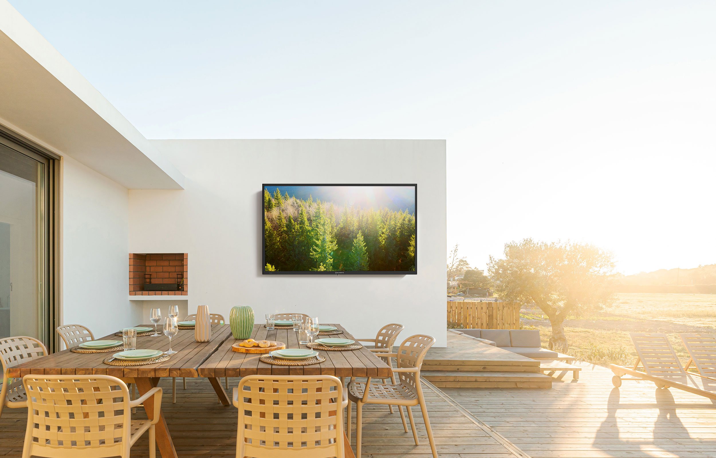 SunBrite outdoor TV mounted on white exterior wall in full bright sunlight above outdoor dining table installed by VIP Smart Homes Seattle