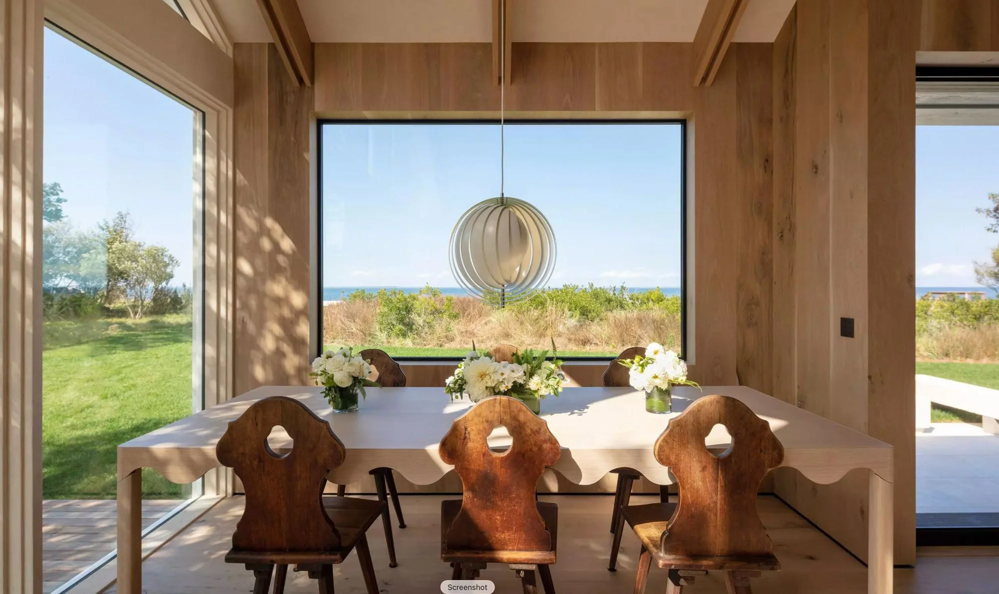 Sun filled modern wood paneled dining room with floor to ceiling ocean view windows demonstrating the natural daylight Lutron Rania mimics | VIP Smart Homes Seattle Bellevue