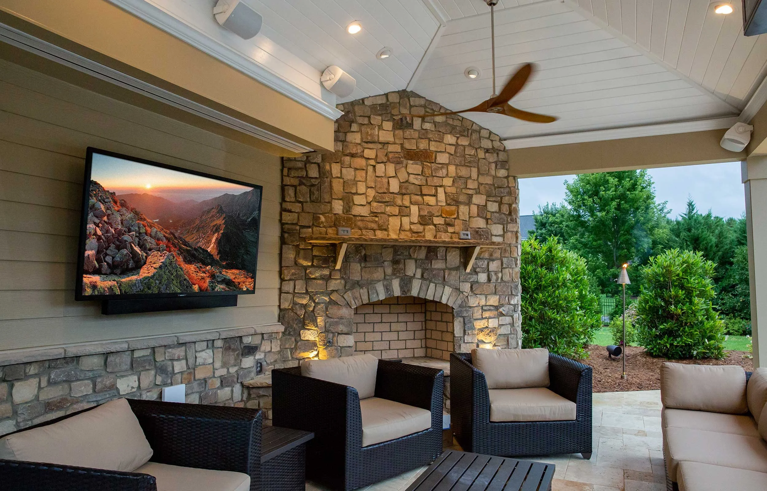 SunBrite outdoor TV installed above stone fireplace in covered patio with ceiling speakers Pacific Northwest installation by VIP Smart Homes
