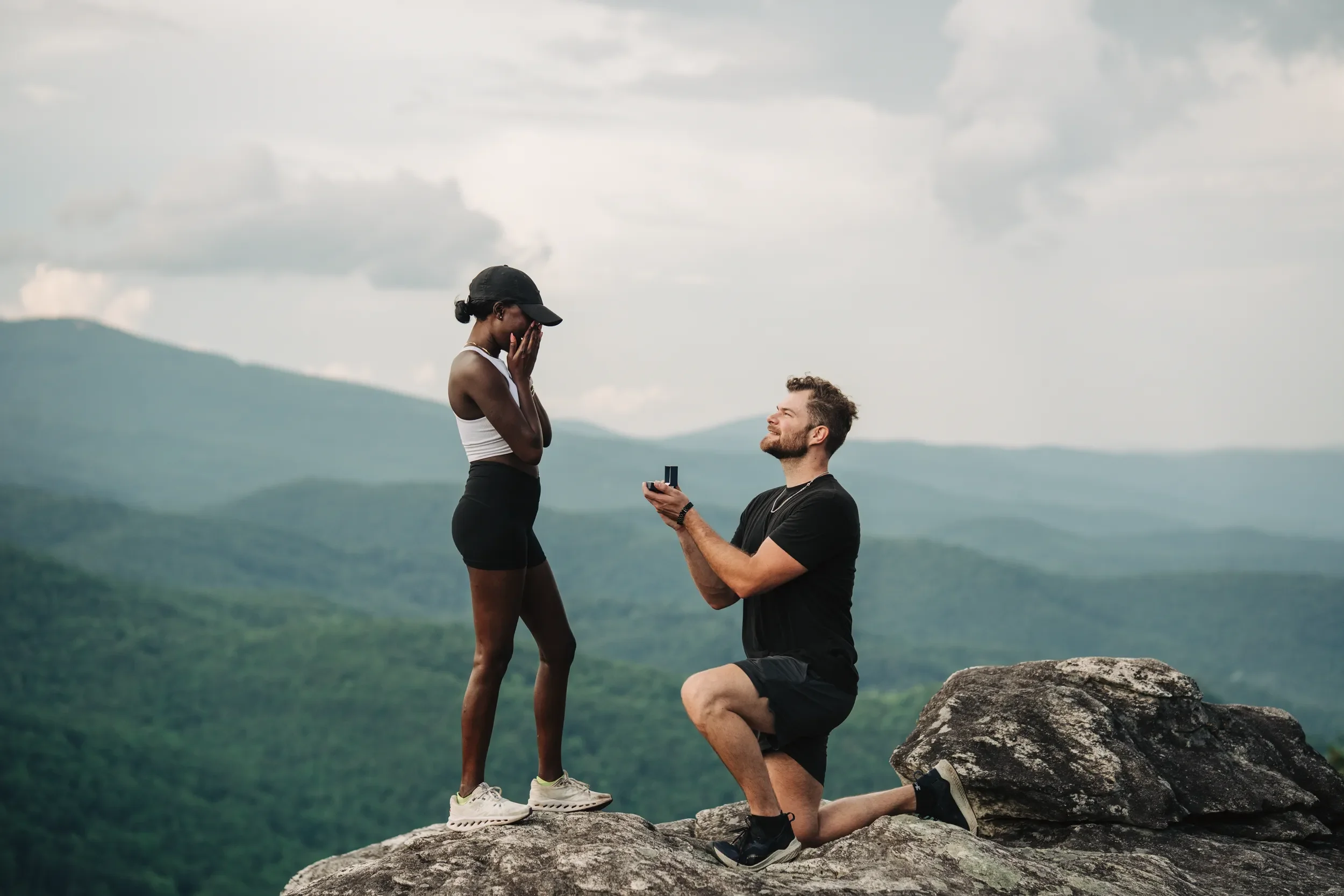 Couple standing together on a rocky mountain overlook before a surprise proposal