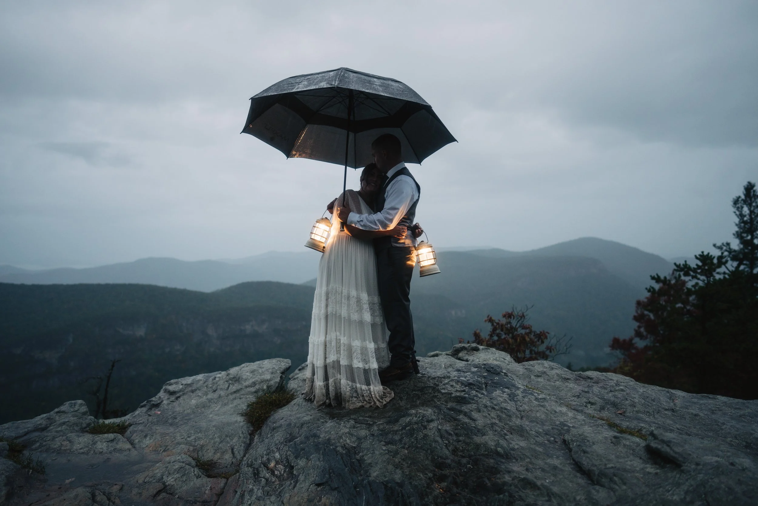 Couple outdoors in the rain sharing an umbrella during a mountain elopement
