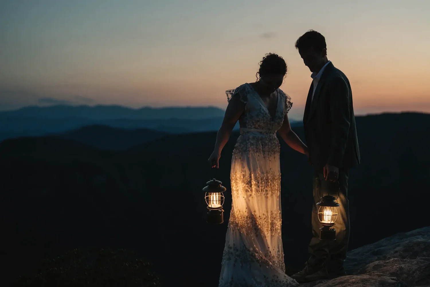 Mackenzie and Michael standing together on Hawksbill Mountain at dusk after sunset.