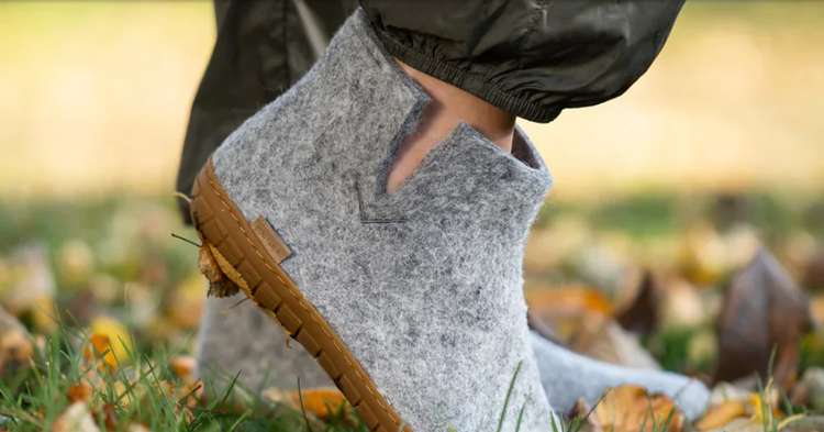 Close-up van twee voeten in grijze wollen sloffen op gras bezaaid met herfstblaadjes
