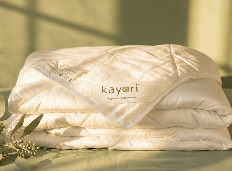 Een opgevouwen ecru-kleurig dekbed met voorop een label met de naam Kayori.
