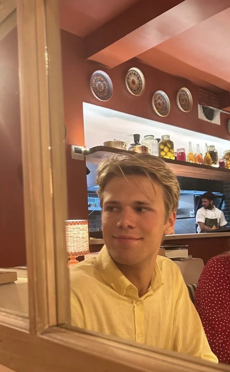 Een jongetje staat met opgestoken duim voor een kledingrek met T-shirts