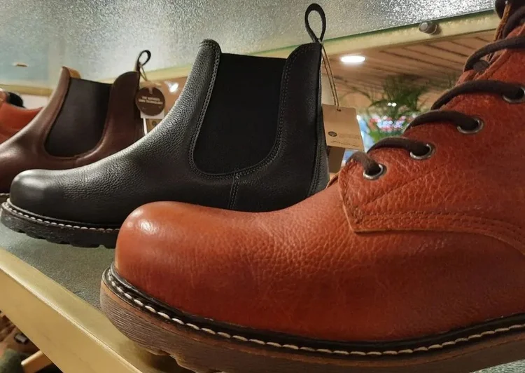 Een rek met daarop een roodbruine leren veterschoen en een zwarte en een donkerbruine enkellaars