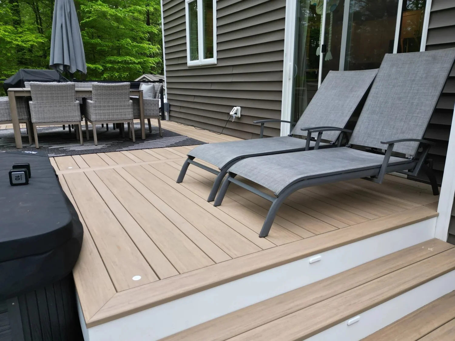 TimberTech deck in Crownsville with broad steps, lounge chairs and outdoor dining beside the house