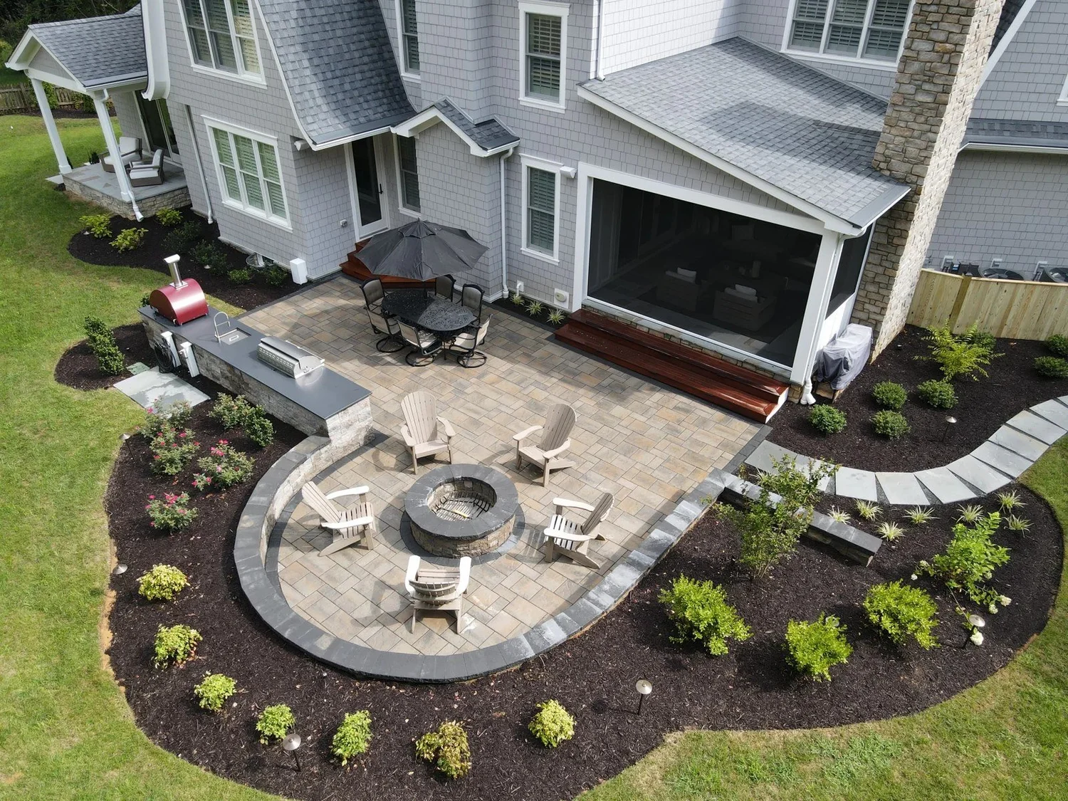 Aerial view of a curved Severna Park patio with outdoor kitchen, red pizza oven and circular firepit seating area