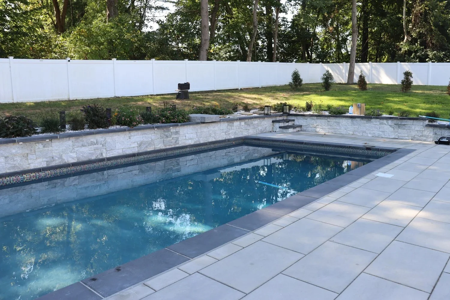 Completed Davidsonville swimming pool with a raised wall, blue water and light gray paver patio