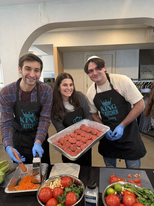 Three volunteers in King of the Kitchen aprons holding up a tray of hand-rolled meatballs