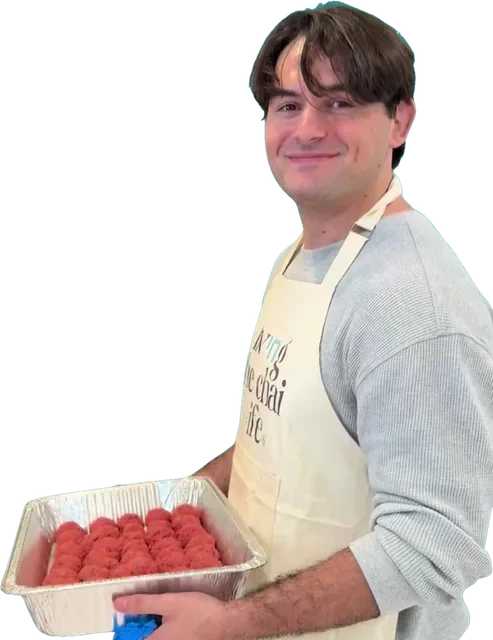 Johnny Ellis, smiling in an apron while holding a tray of meatballs he rolled by hand