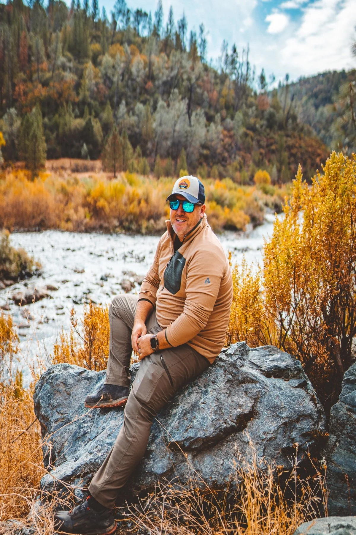 Greg Bodene seated beside a river among golden autumn foliage
