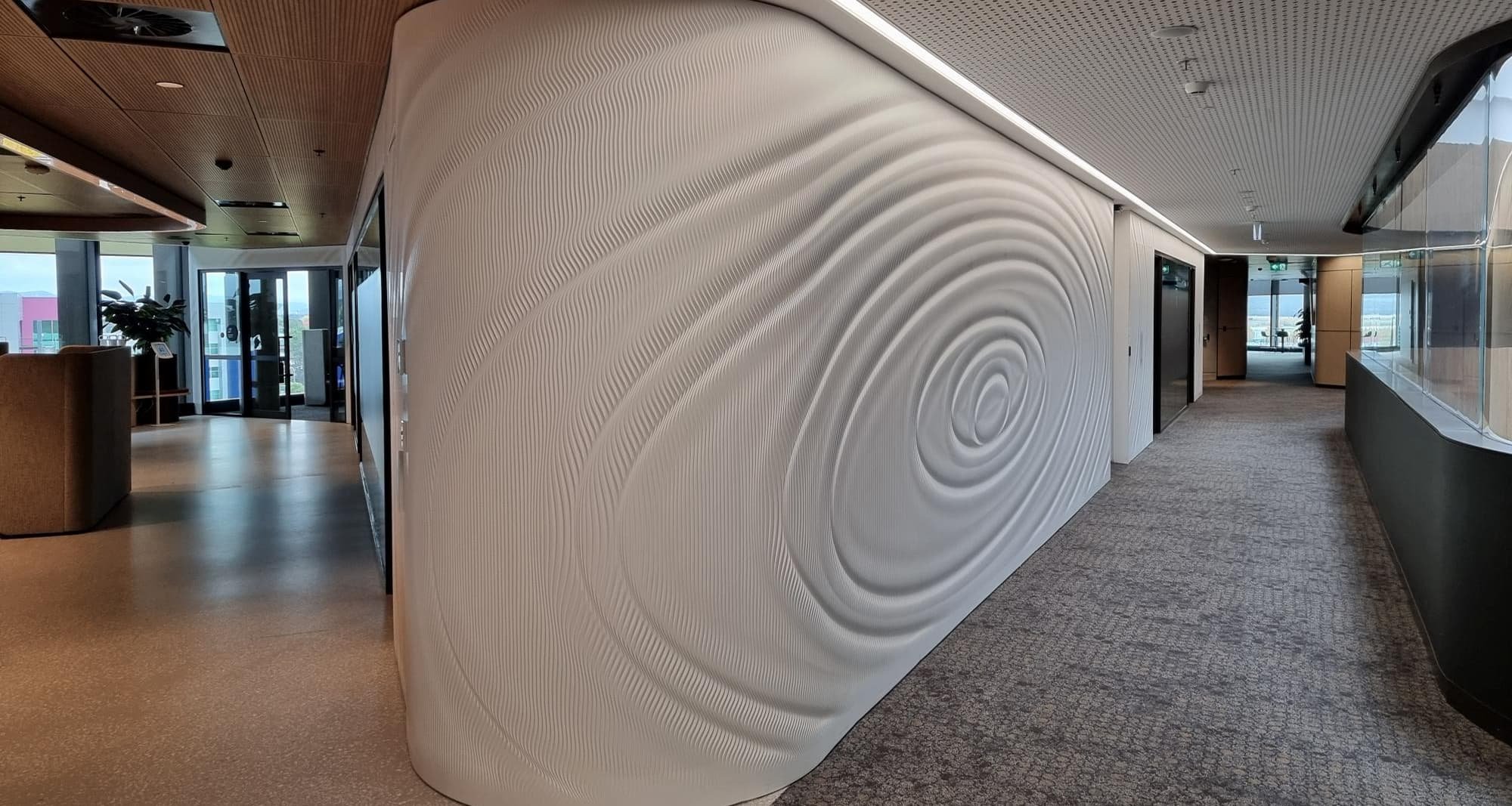 A white carved wall with an orbit design that curves around the corner of the Deloitte corporate office.