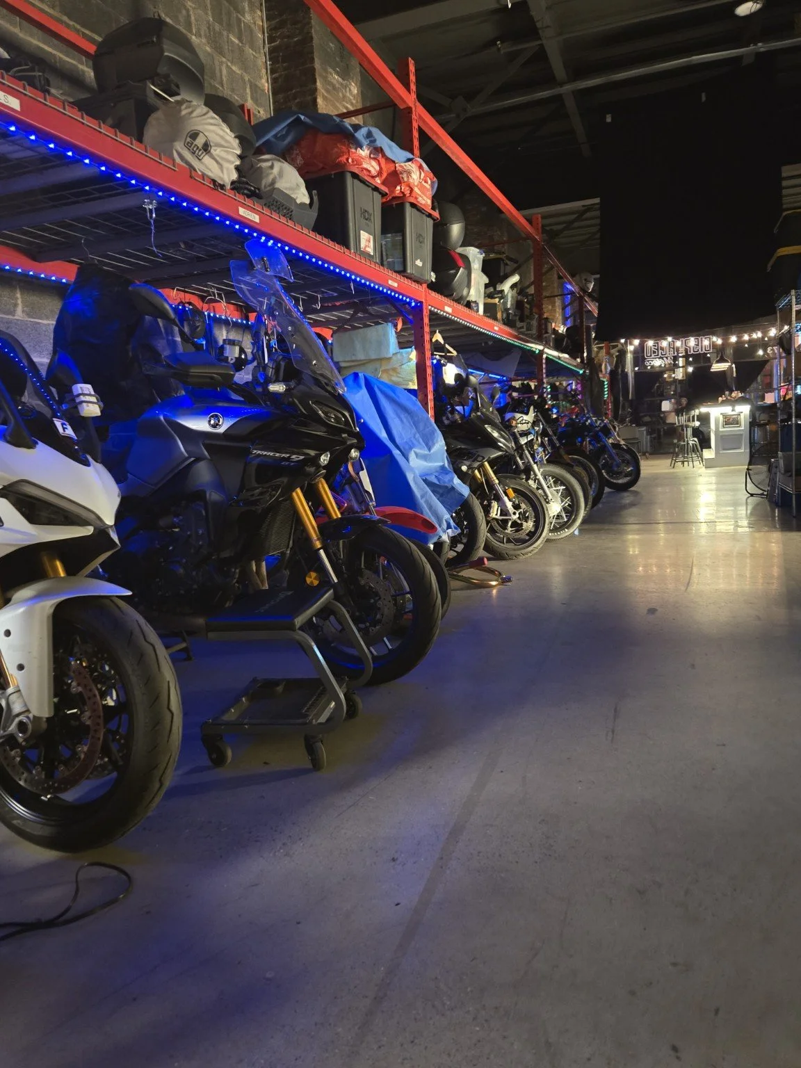 View down the garage aisle with a row of parked motorcycles at Displaced Motoco