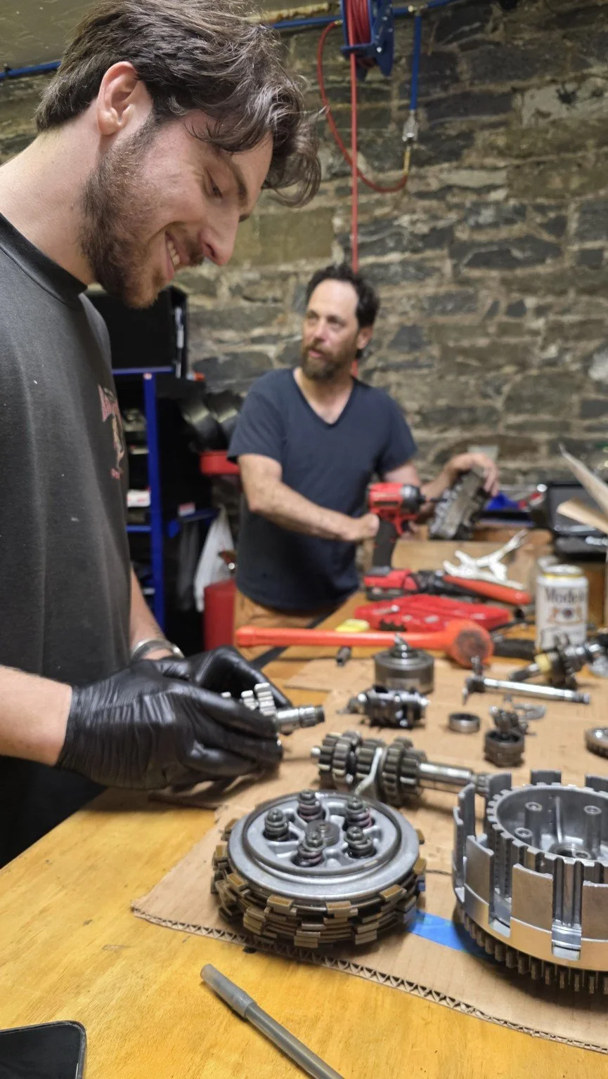 Smiling participant handling motorcycle engine parts at the workbench