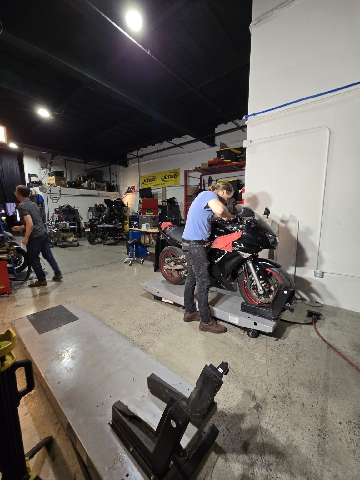 Member working on a motorcycle on a lift in the Displaced workshop