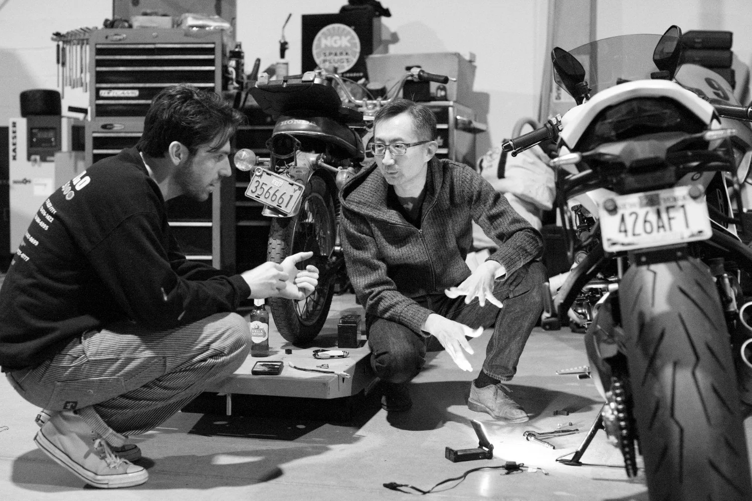 Two people discussing a motorcycle in the workshop, photographed in black and white