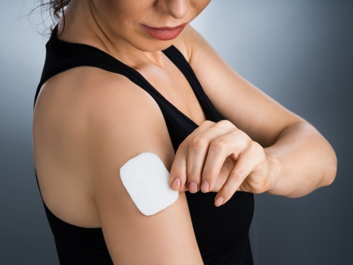 Woman applying bioidentical hormone patch on upper arm for hormone optimization and BHRT treatment