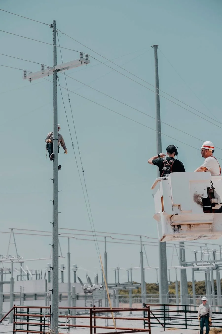 People's Electric Cooperative linemen working at a substation, with one climbing a utility pole and another in a bucket truck.