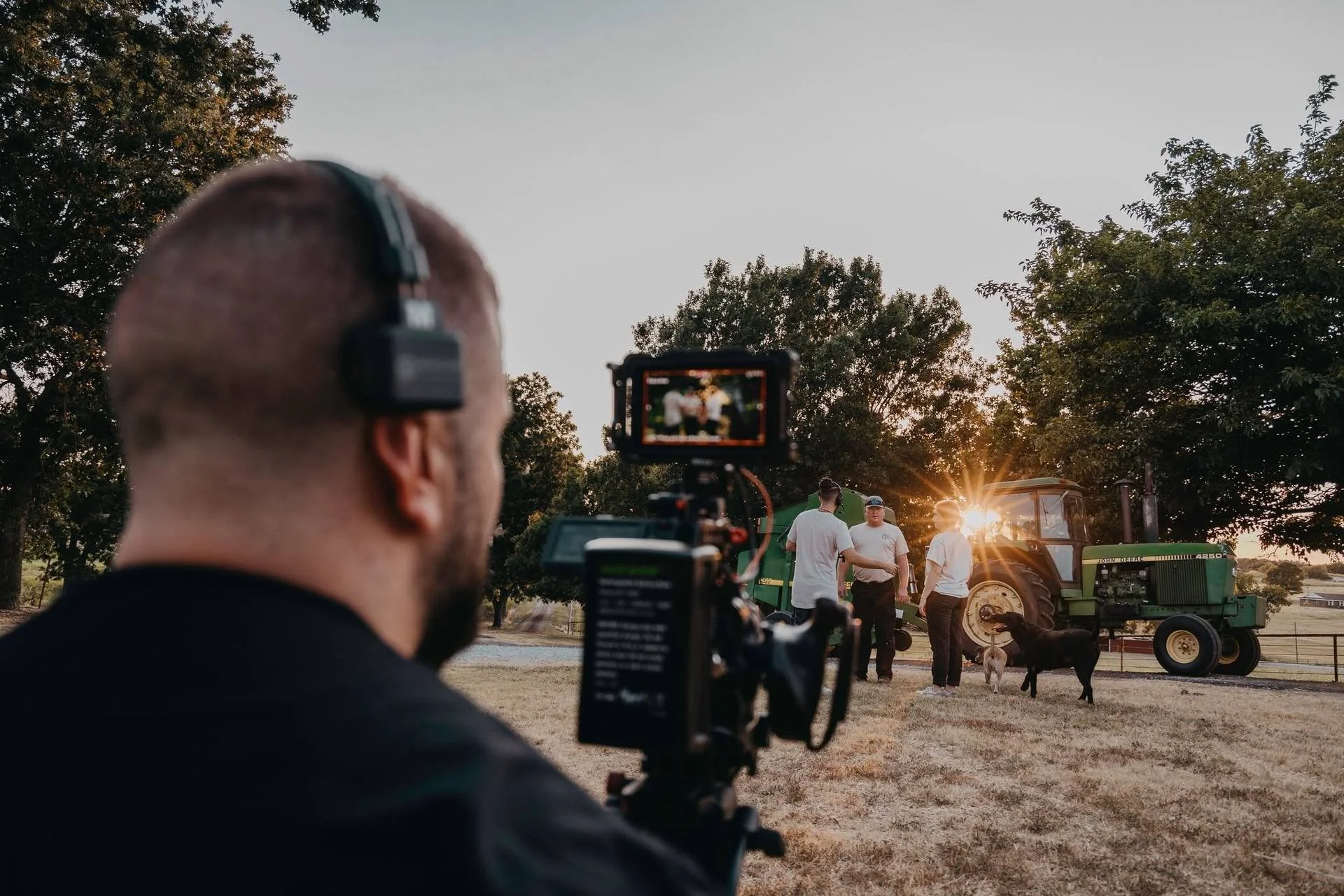 A Hyped Visuals camera operator films People's Electric Cooperative crew members beside a tractor at sunset during production of the brand film