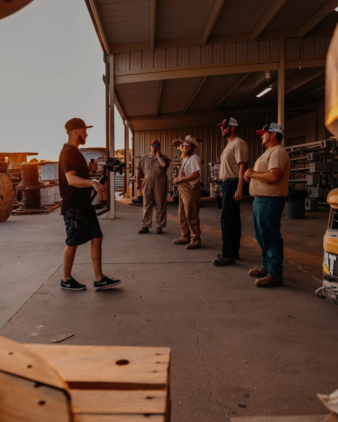 A Hyped Visuals director briefs a lineup of four People's Electric Cooperative crew members at a materials yard at sunset