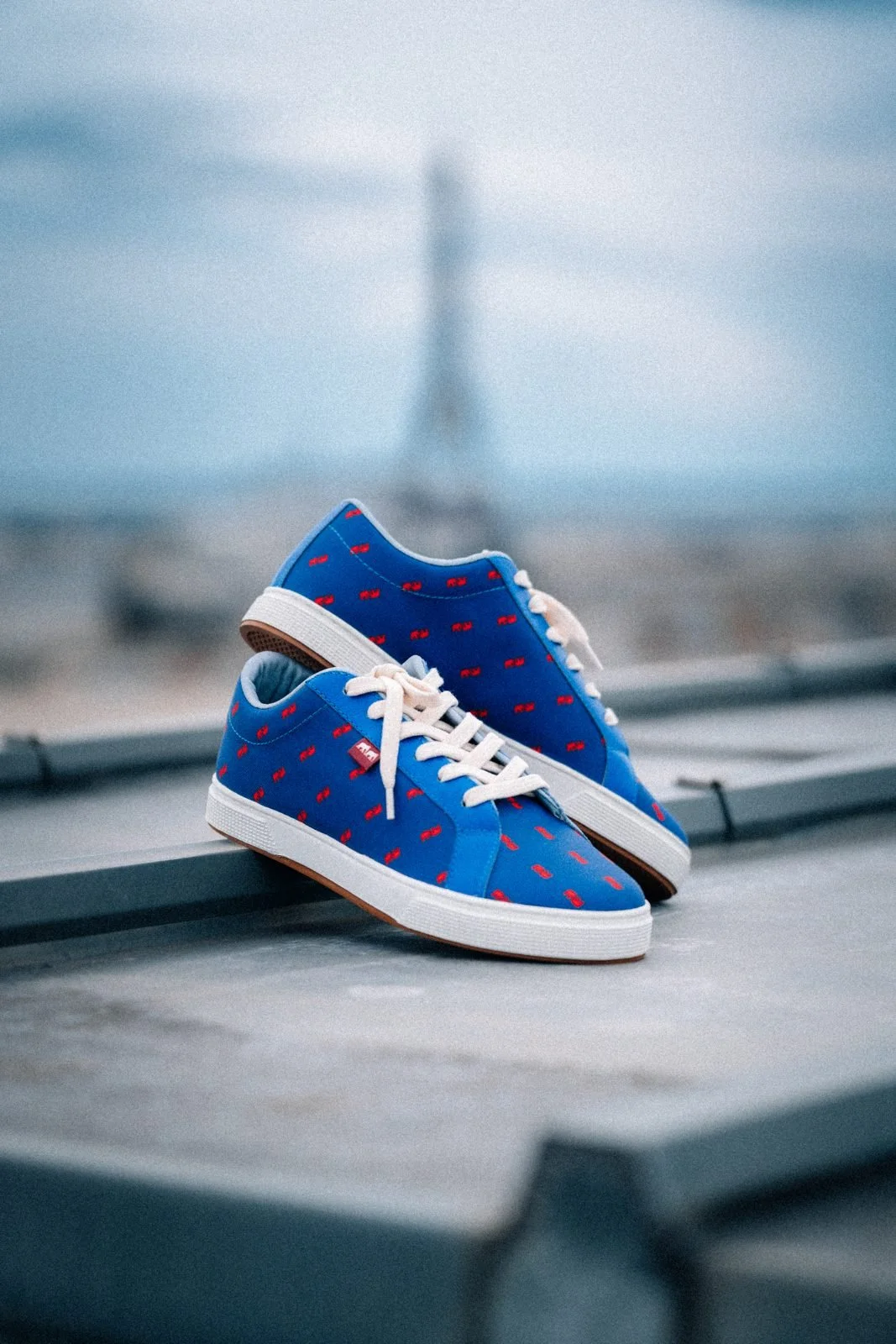 Sneakers bleues Twins for Peace posées sur un toit parisien face à la tour Eiffel, photo produit mode
