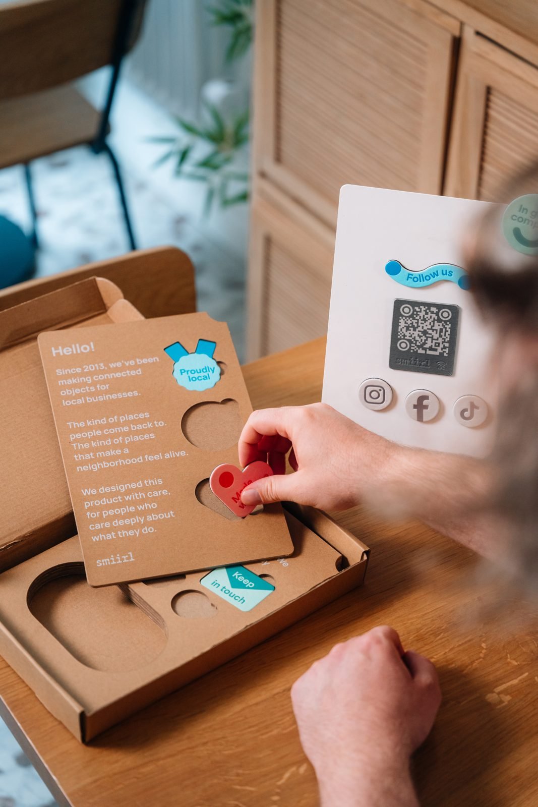 Déballage du kit présentoir Smiirl sur une table en bois : boîte, jeton et présentoir avec QR code